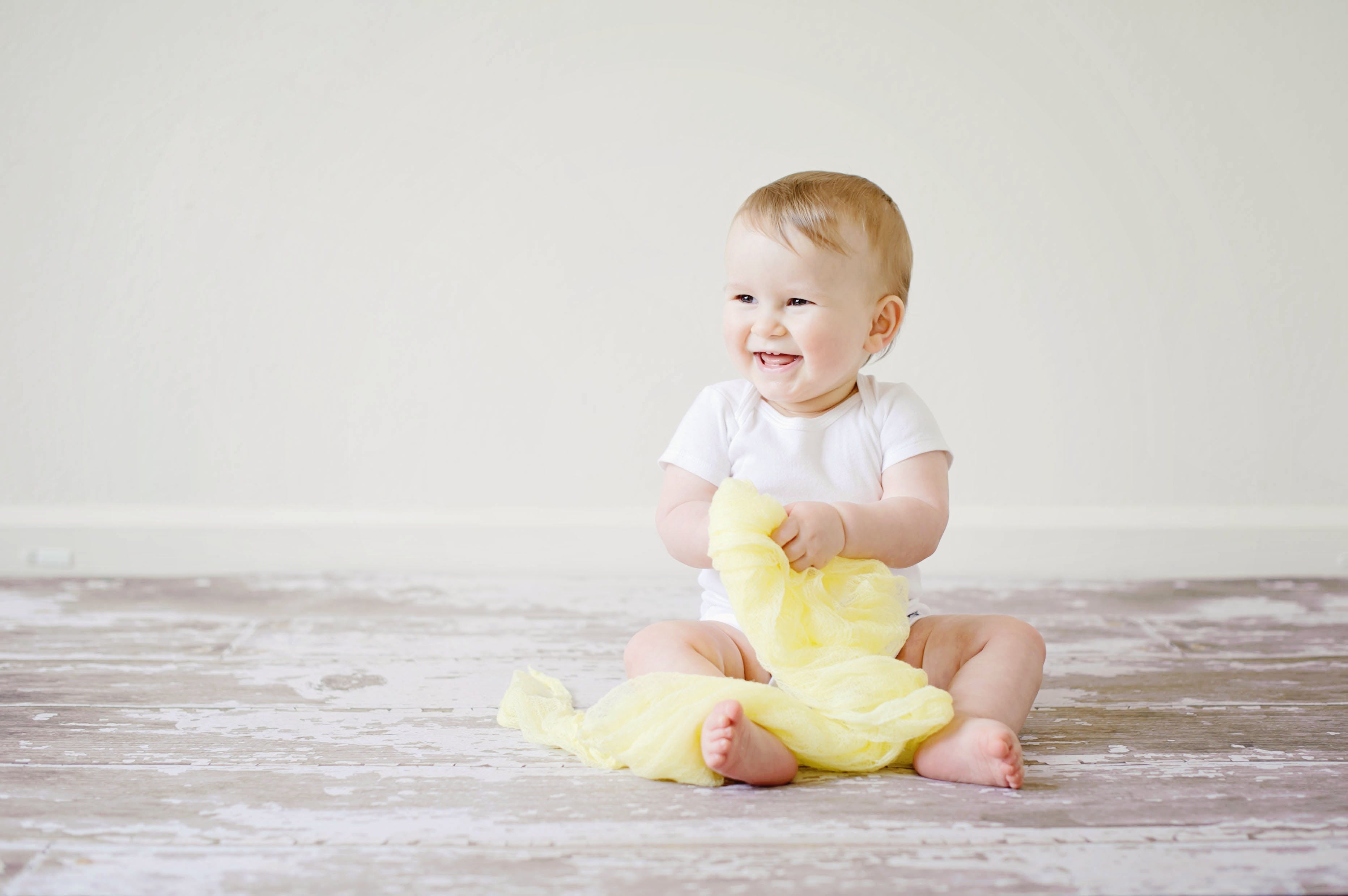 baby sat up laughing and holding yellow blanket